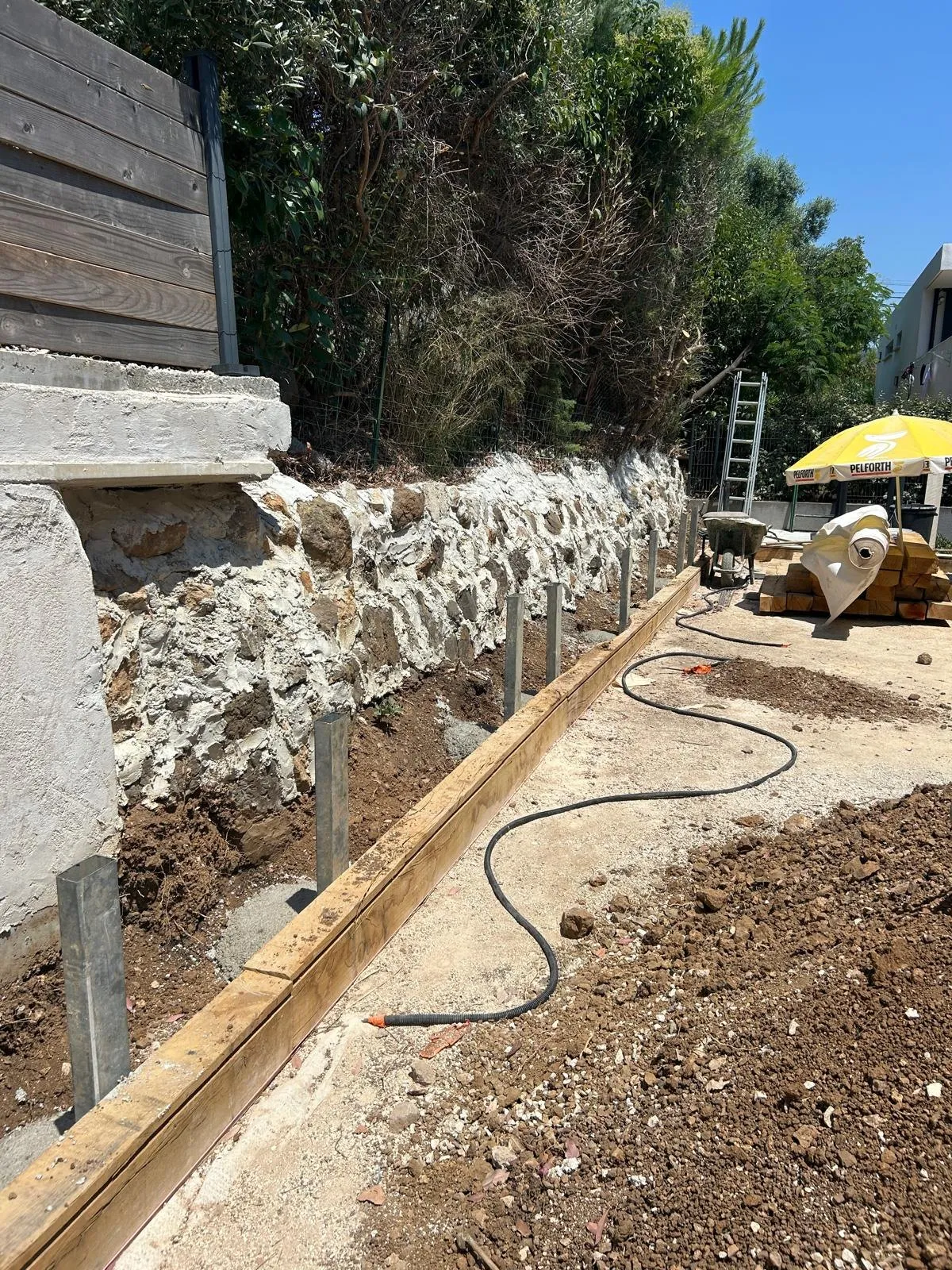Bordure en bois et soutènement en cours le long d’un mur en pierre